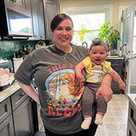 TheFirstLifestyle 34 Customer photo of a mom wearing a grey This Mama Is A Rebel graphic tee while holding her baby