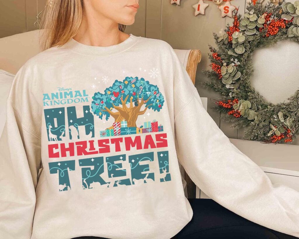 Christmas at Animal Kingdom Secrets Every Traveler Needs for 2027 24 Woman relaxing indoors with holiday ceramic mug wearing ivory tree of life Christmas crewneck sweatshirt