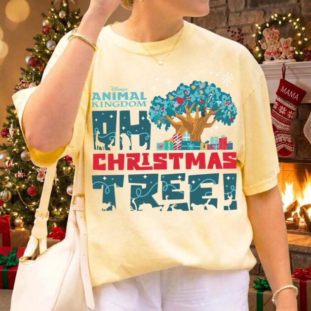 Animal Kingdom Oh Christmas Tree Shirt for Holiday Vacations 15 Woman wearing butter yellow decorated tree of life tee by stone fireplace with Christmas stockings