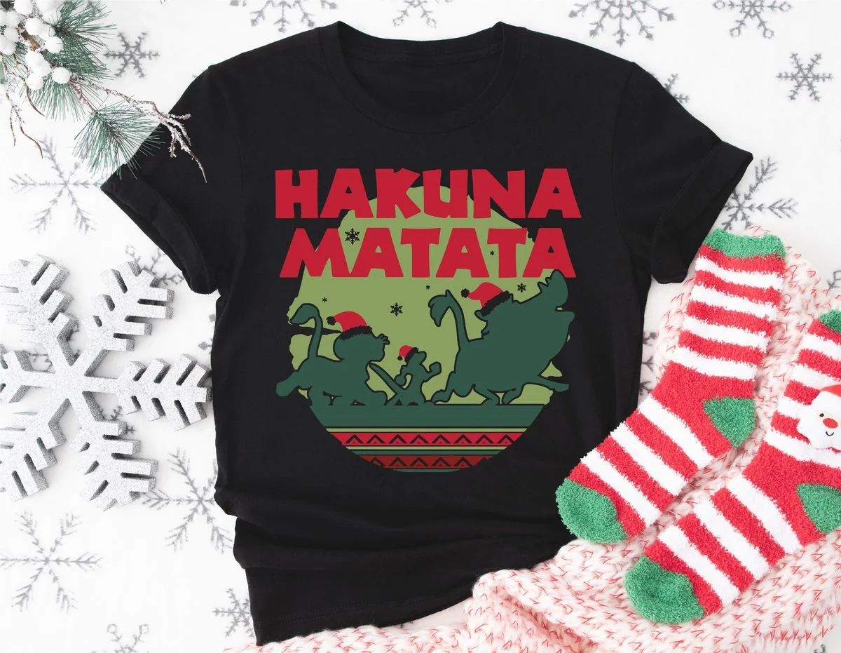 Lion King Hakuna Matata Christmas Sweatshirt with Nordic Art 4 Flat lay of black lion king hakuna matata t-shirt on white wooden planks with pine cones and holiday greenery