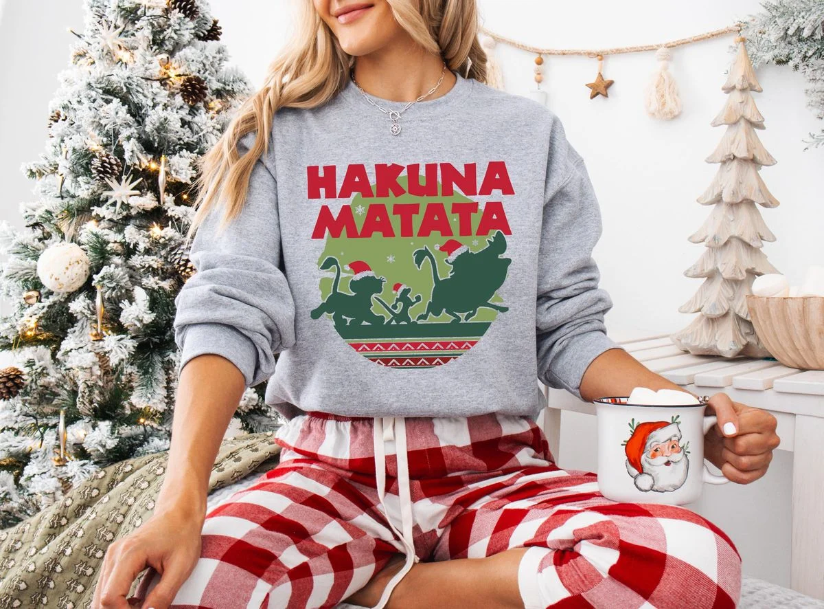 Lion King Hakuna Matata Christmas Sweatshirt with Nordic Art 3 Smiling model indoors wearing heather grey santa simba silhouette crewneck with Nordic Fair Isle savanna artwork