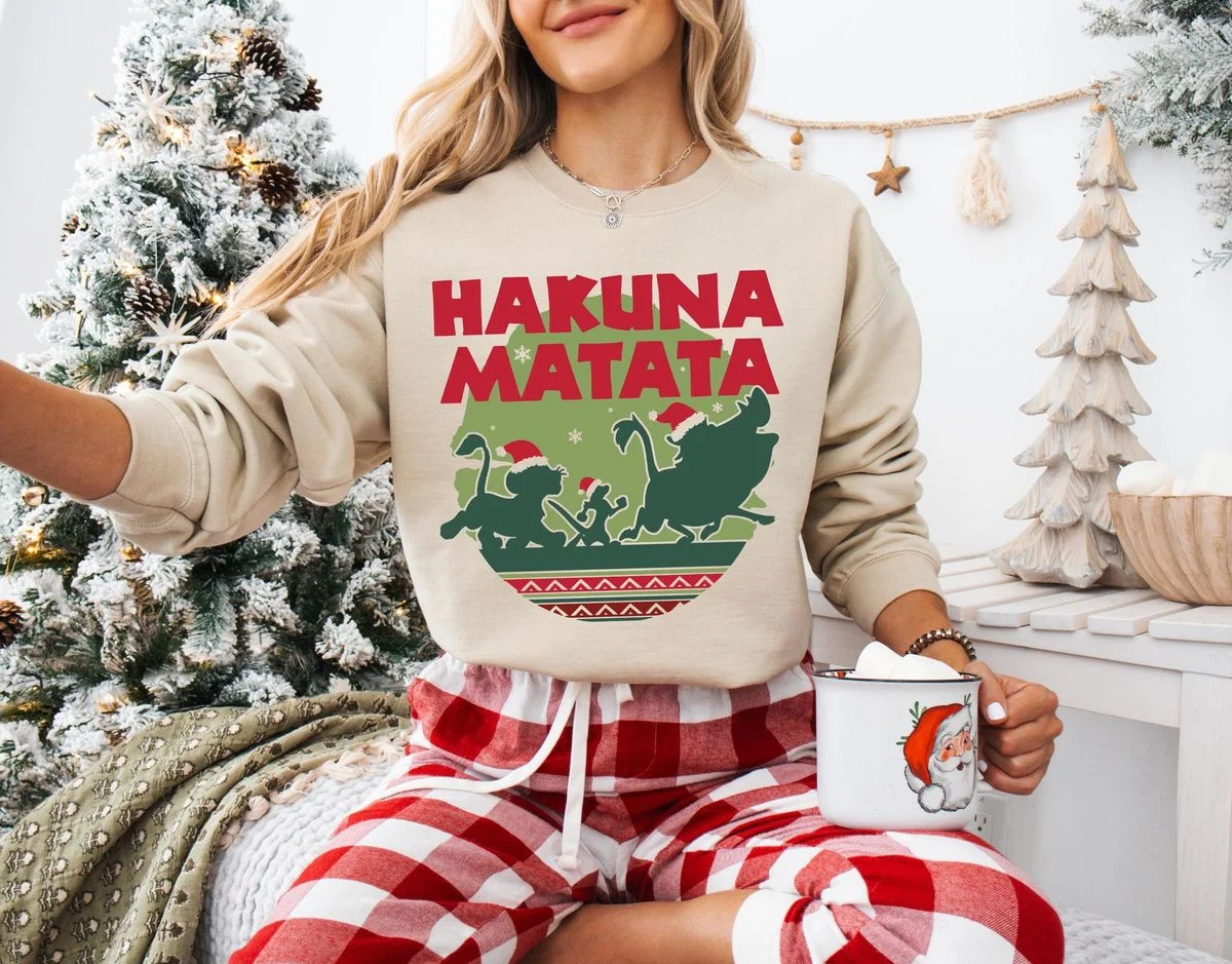 Lion King Hakuna Matata Christmas Sweatshirt with Nordic Art 7 Woman in cozy living room wearing sand tan lion king hakuna matata christmas sweatshirt with red buffalo check lounge pants
