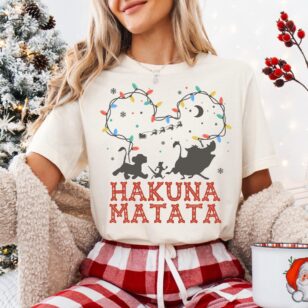 Woman wearing ivory lion king hakuna matata christmas t-shirt with buffalo plaid pajama pants holding holiday mug near tree