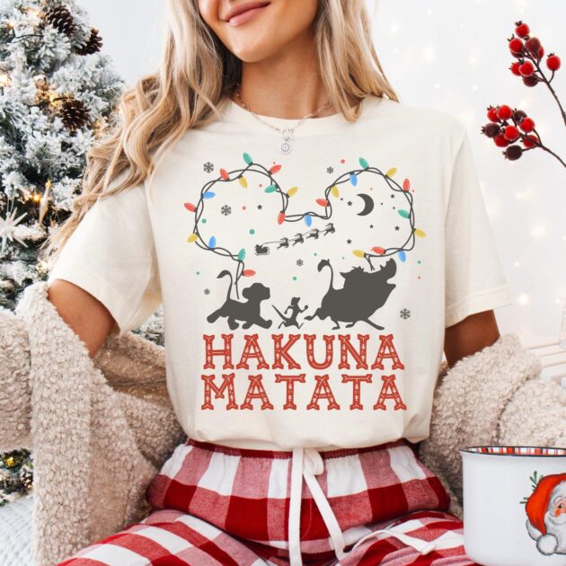 Lion King Hakuna Matata Christmas T-Shirt with Mickey Light Art 12 Woman wearing ivory lion king hakuna matata christmas t-shirt with buffalo plaid pajama pants holding holiday mug near tree