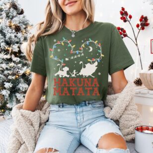 Lion King Hakuna Matata Christmas T-Shirt with Mickey Light Art 6 Brunette model wearing olive green fair isle lion king tee in front of illuminated holiday background