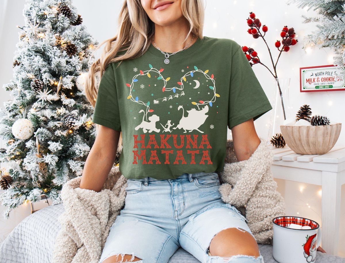 Lion King Hakuna Matata Christmas T-Shirt with Mickey Light Art 11 Brunette model wearing olive green fair isle lion king tee in front of illuminated holiday background