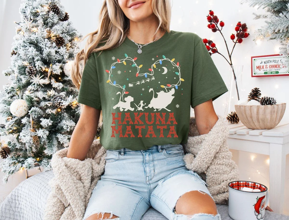 Lion King Hakuna Matata Christmas T-Shirt with Mickey Light Art 2 Brunette model wearing olive green fair isle lion king tee in front of illuminated holiday background