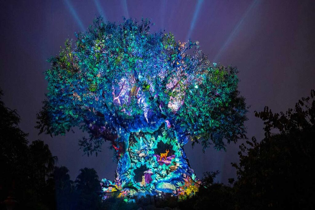 Christmas at Animal Kingdom Secrets Every Traveler Needs for 2027 12 The Tree of Life lit up in icy blue projection lights showing winter animals and light beams shooting into the night sky