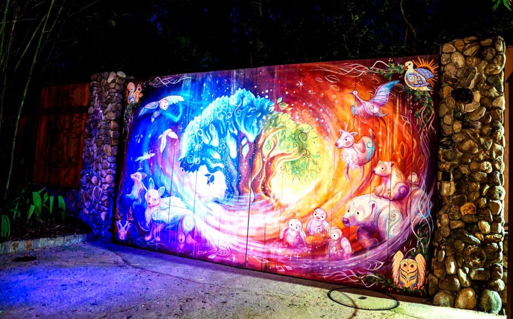 Christmas at Animal Kingdom Secrets Every Traveler Needs for 2027 27 A painted wooden holiday mural of the Tree of Life surrounded by glowing winter animals like polar bears, foxes, and deer framed by stone pillars at night