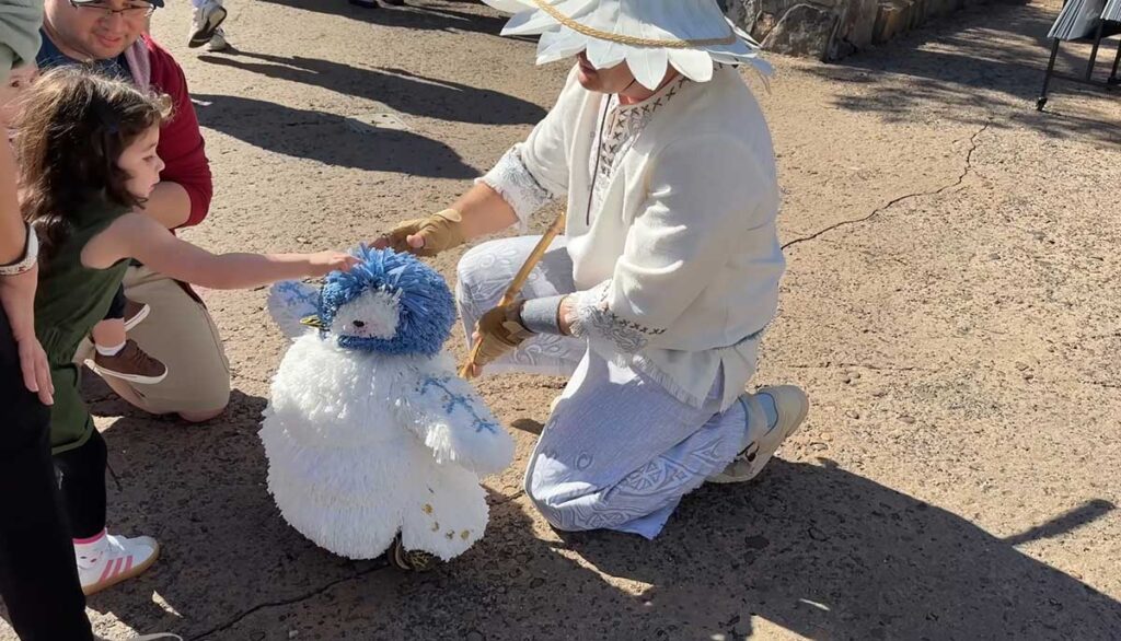 Christmas at Animal Kingdom Secrets Every Traveler Needs for 2027 8 A young girl reaching out her hand to touch the blue crest of the artisan penguin puppet on Discovery Island