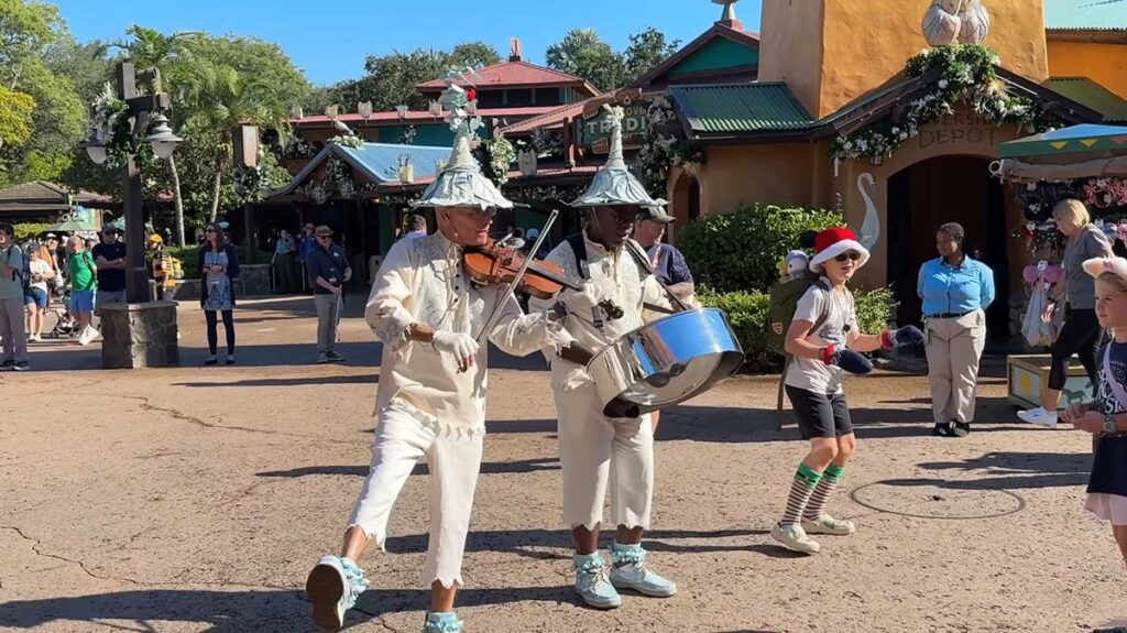 Christmas at Animal Kingdom Secrets Every Traveler Needs for 2027 9 Two street musicians in white holiday costumes playing violin and steel pan drums on Discovery Island outside Riverside Depot